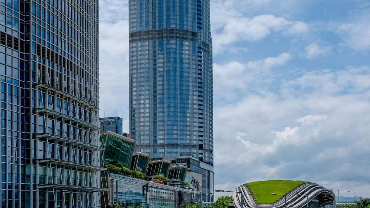 Bright daytime view of modern Hong Kong office towers under a blue sky with a green-roofed building — an open, accessible business hub for foreign founders