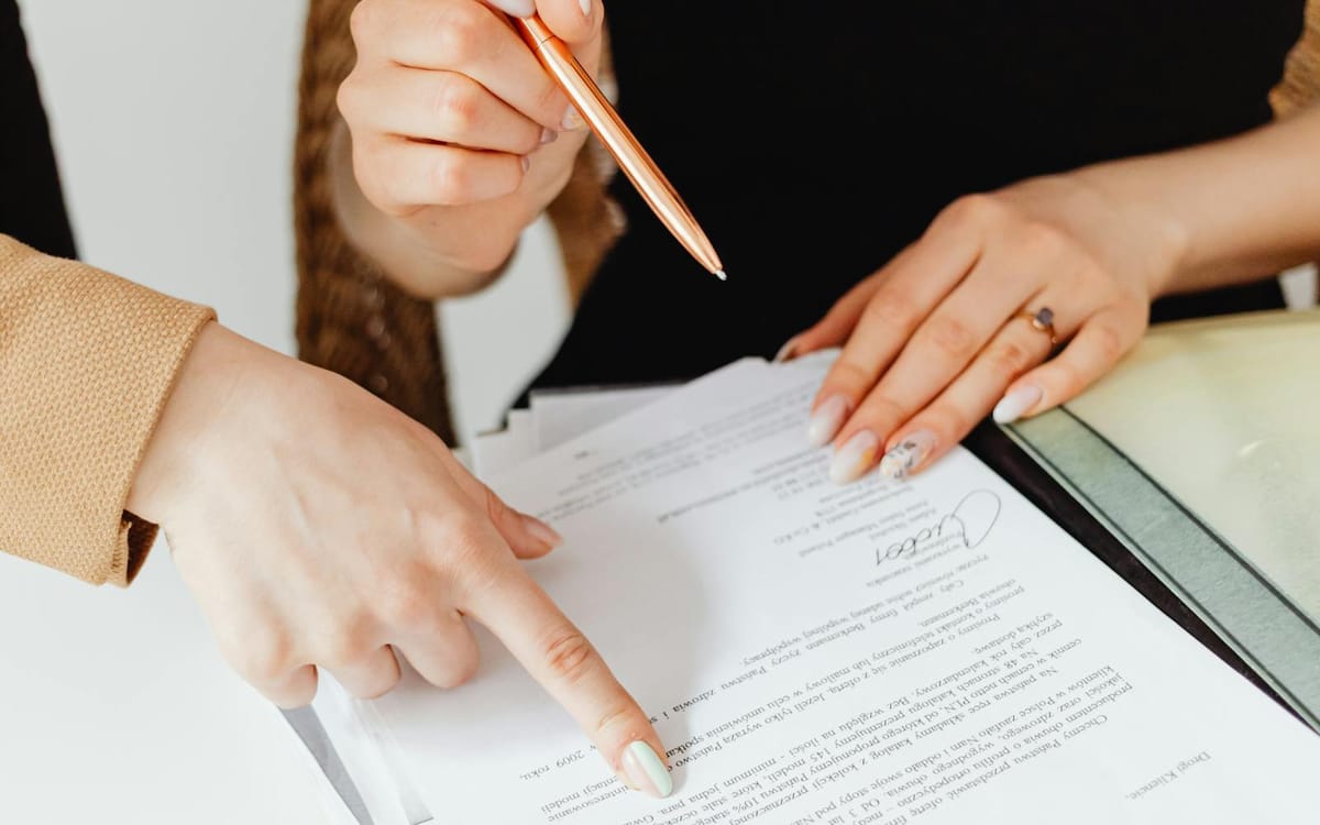 Deux personnes examinent et signent ensemble un contrat à un bureau, avec un classeur et un café — un fondateur qui officialise la prochaine étape d'une entreprise en croissance